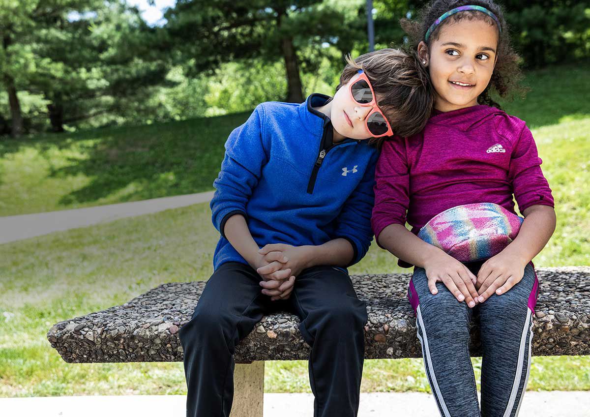 Boy Wearing Under Armour Quarter-Zip And Girl Wearing Adidas Shirt Sitting On Bench
