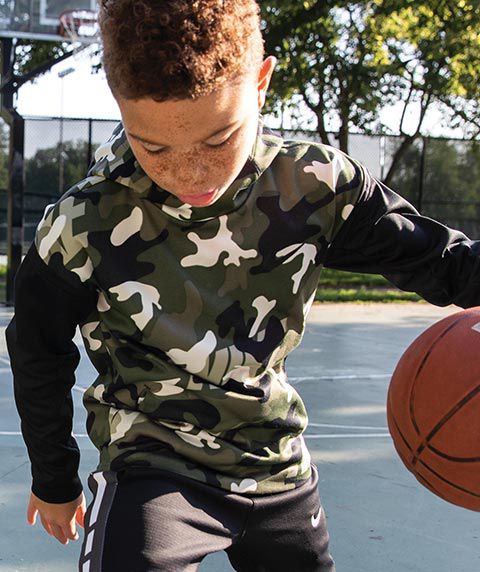 A kid playing basketball wearing Nike Boys' Therma Camo Printed Hoodie, Nike Boys' Dri-FIT Therma Elite Pants and Nike Kyrie Flytrap II Basketball Shoes.